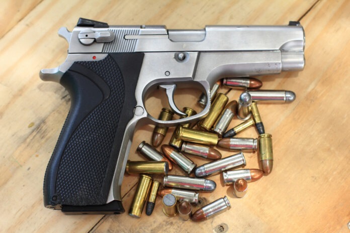Eine Waffe mit Munition liegt auf einem Holztisch.