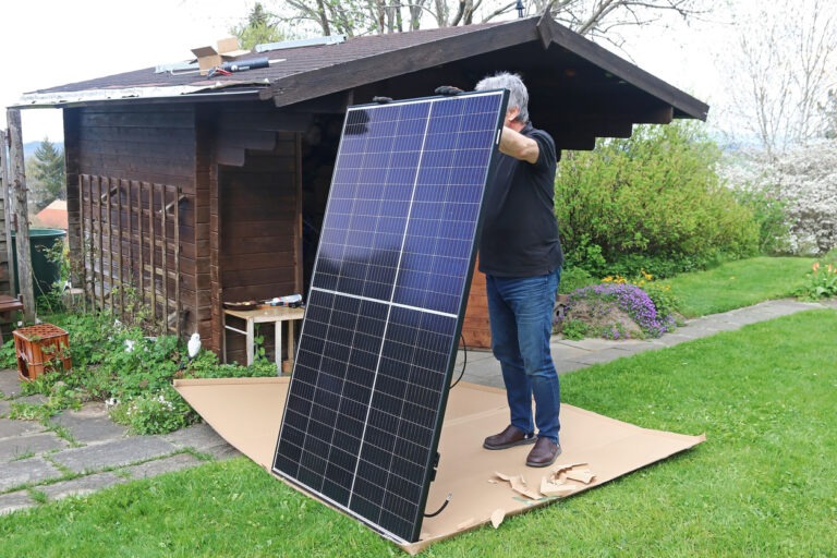 Ein Mann hält ein Solarmodul einer Solar-Anlage im Garten.