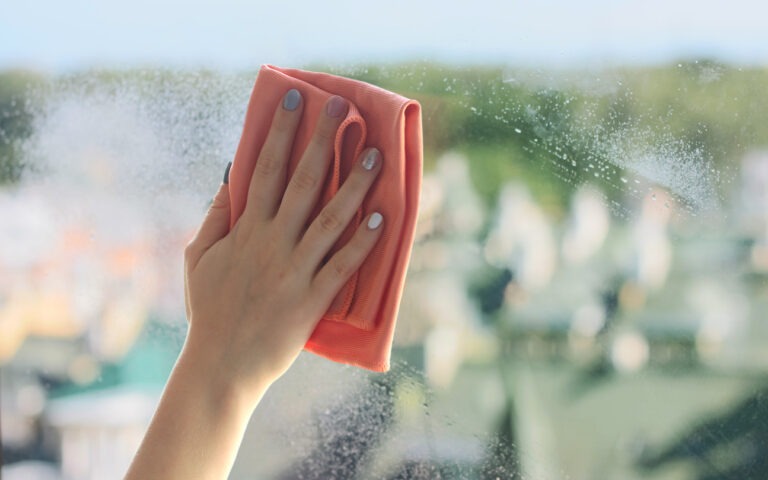 Eine weibliche Hand fährt mit einem Wischlappen über ein Fenster, um es zu reinigen.