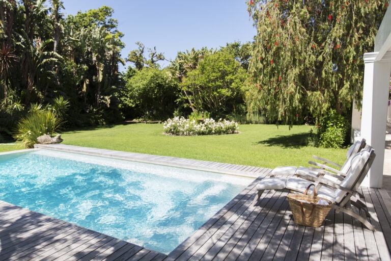 Eine Liege steht an einem schön angelegten Pool in einem weitläufigen Garten.