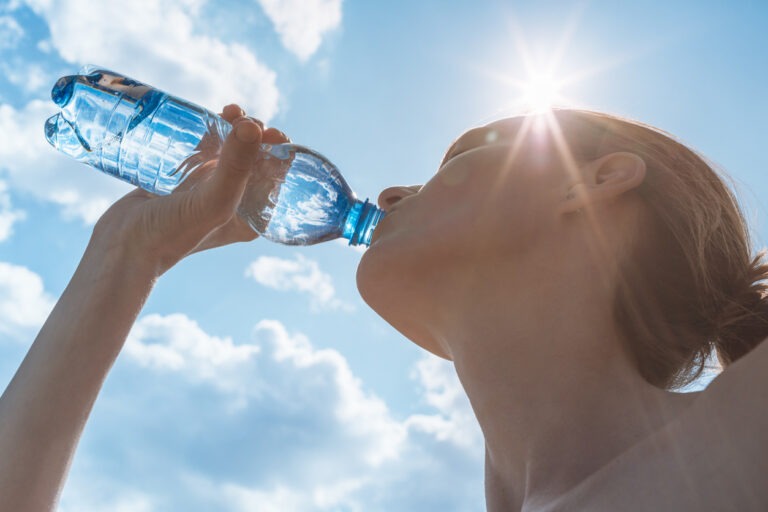 Eine Frau trinkt im Sommer bei großer Hitze Wasser aus einer Flasche.