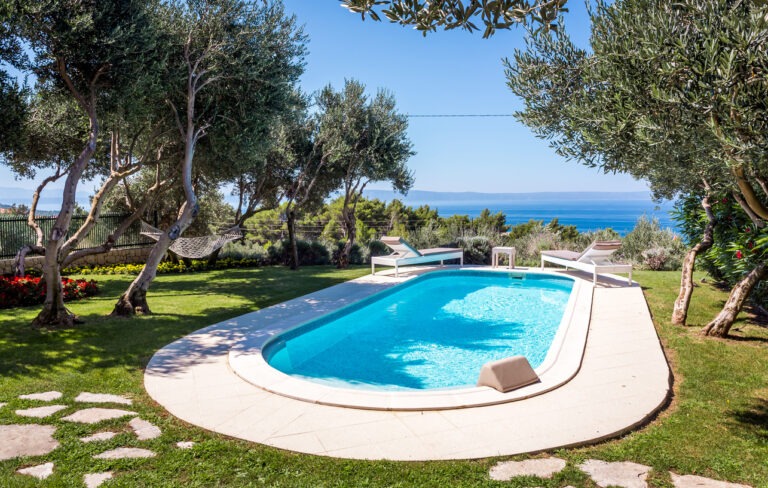 Ein gepflegter Garten mit einem schönen Pool, bietet Blick auf das darunter liegende Meer.