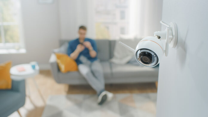 Ein Mann sitzt auf dem Sofa während eine Kamera den Raum überwacht.