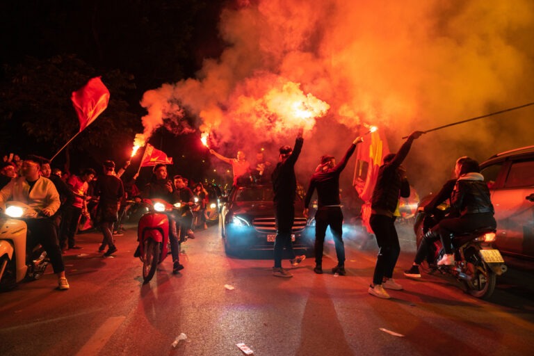 Eine Gruppe Fußballfans feiert mit einem Autokorso und Fahnen auf der Straße.