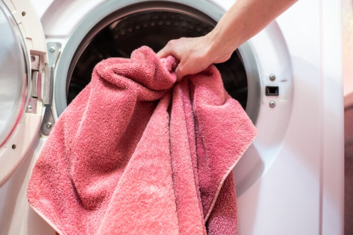 Ein rotes Handtuch wird in die Wäschetrommel einer Waschmaschine gegeben.