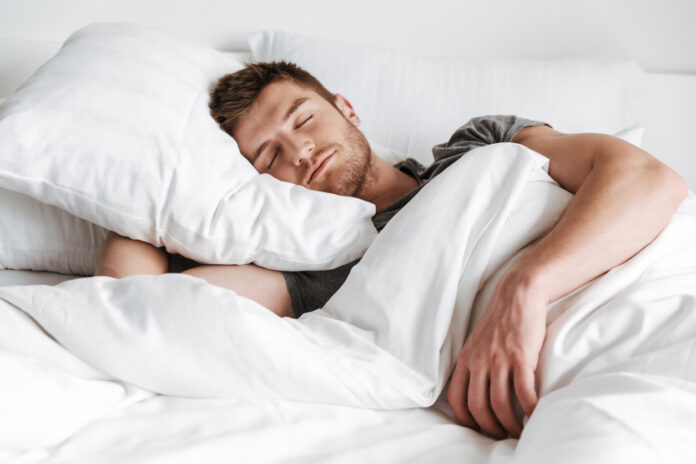 Ein junger Mann schläft friedlich in seinem Bett mit weißen Laken und Bezügen.
