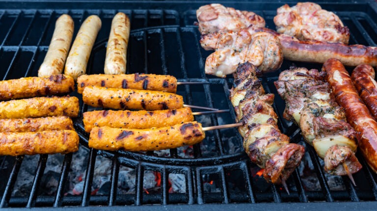 Neben Fleisch und Spießen liegen vegane Grillwürstchen auf dem Grill.