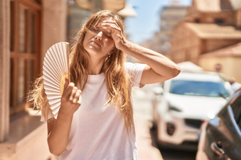 Eine junge Frau fächelt sich mit einem Fächer im Sommer und in der Hitze Luft zu.