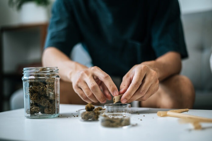 Ein Mann hat ein Glas Cannabis vor sich stehen und sitzt auf seiner Couch.