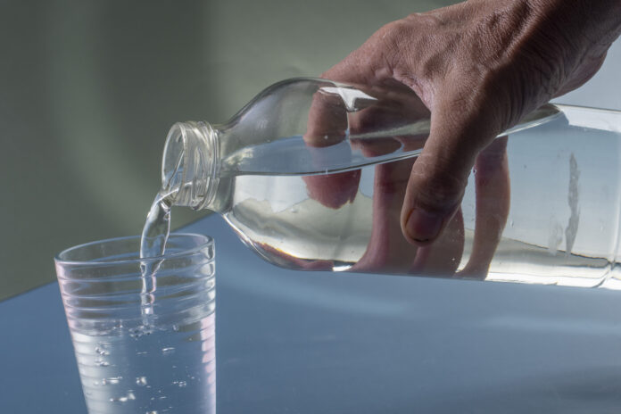 Ein Mann gießt Wasser aus einer PET-Flasche in ein Glas.