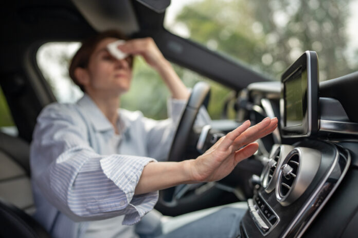 Eine Frau schwitzt im Auto und testet die Temperatur an der Lüftung mit der Hand.