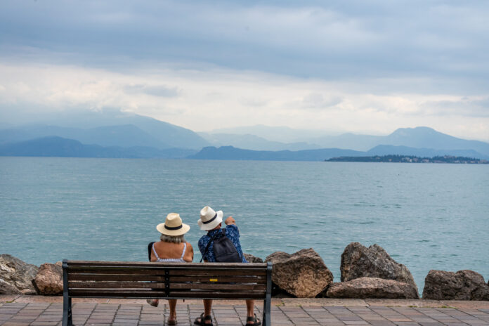 Ein älteres Paar sitzt auf einer Bank und blickt auf den Gardasee.