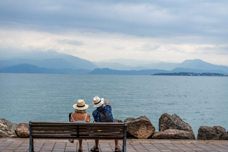 Ein älteres Paar sitzt auf einer Bank und blickt auf den Gardasee.