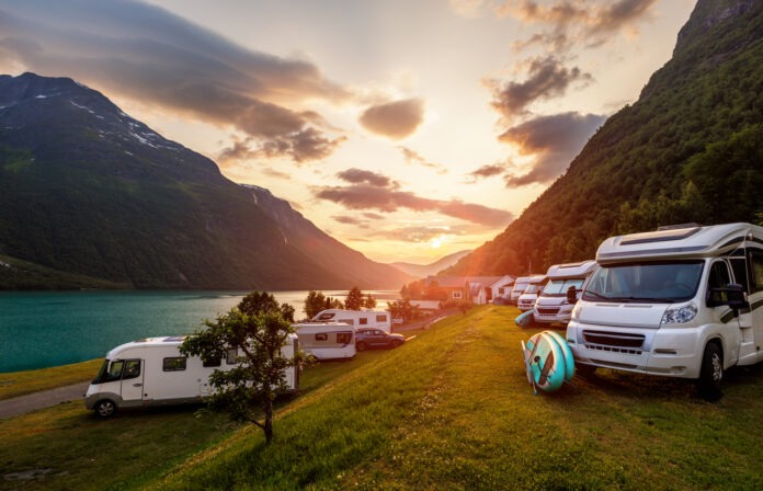 Eine Reihe Wohnmobile stehen auf einem idyllischen Campingplatz an einem See.