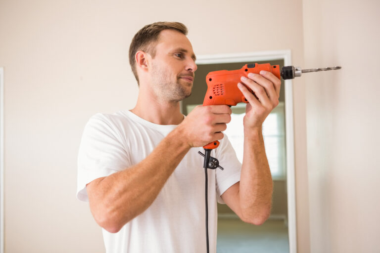 Ein Mann in einem weißen T-Shirt bohrt mit einer Bohrmaschine in die Wand.