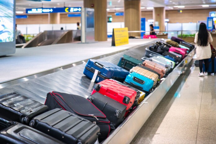 Reisende warten am Flughafen am Gepäckband auf ihren Koffer.