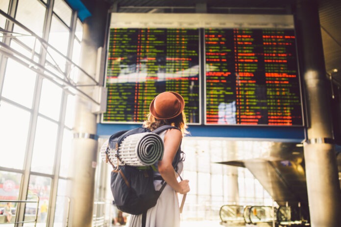 Eine Frau mit Rucksack steht vor einer Anzeigentafel und überprüft ihren Flug.