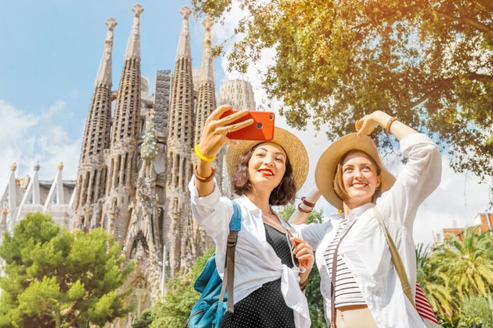 Zwei Touristinnen fotografieren sich in Barcelona, Spanien vor einer Kathedrale.