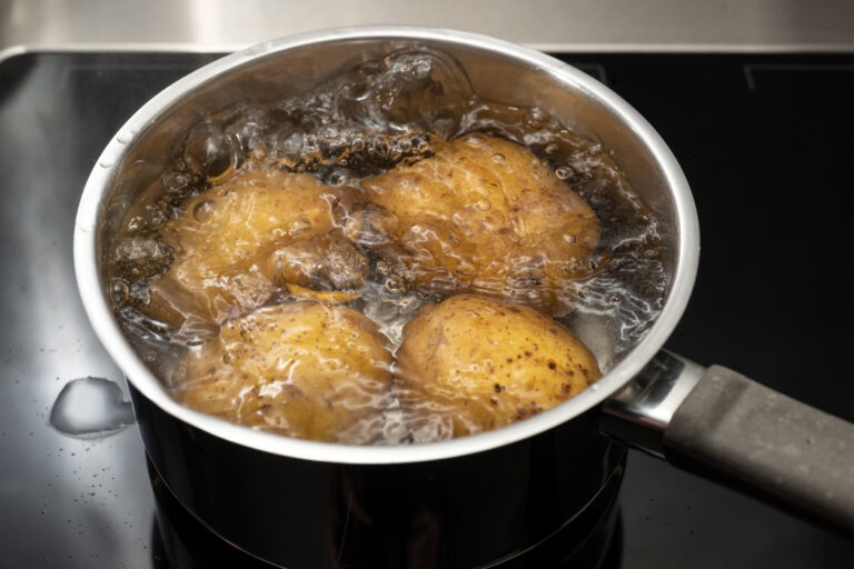 Kartoffeln liegen in kochendem Wasser in einem Topf, welcher auf der Herdplatte steht.