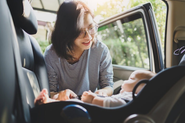 Eine junge Mutter schnallt ihr Baby im Kindersitz im Auto an.