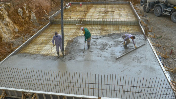 Handwerker gießen eine Bodenplatte aus Beton auf einer Baustelle.