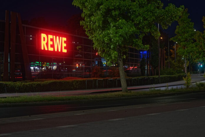 Ein Rewe mit beleuchtetem Schild bei Nacht.