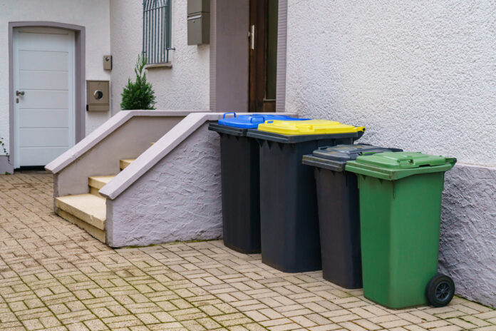 Vier Mülleimer verschiedener Größe stehen nebeneinander an der Hauswand.