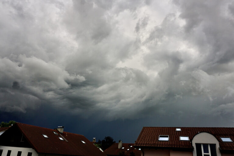 Über einem Wohngebiet zieht ein Unwetter mit dicken, dunklen Wolken auf.