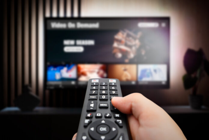 Ein Mann wählt mit der Fernbedienung auf seinem TV-Gerät ein Programm oder einen Streamingdienst aus.