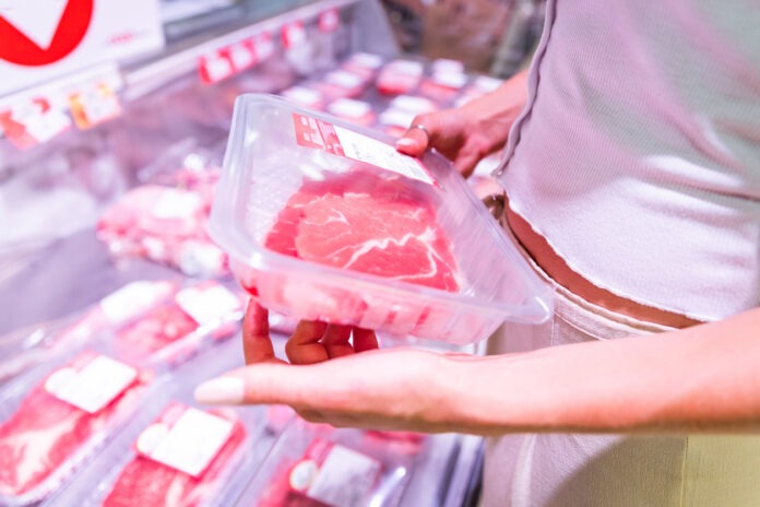 Eine Frau hält verpacktes Fleisch von der Fleischtheke in einem Supermarkt in der Hand.