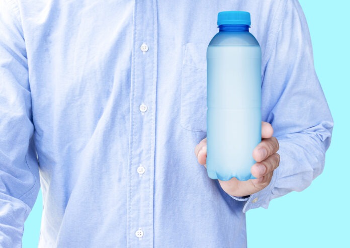 Ein Mann in einem blauen Hemd hält eine Flasche mit gekühltem Wasser in der Hand.