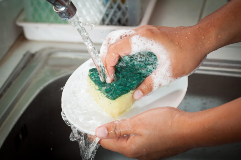 Eine Frau reinigt Geschirr mit einem Schwamm im Spülbecken.