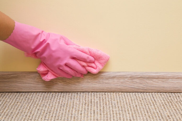 Eine Frau mit rosafarbenen Putzhandschuhen reinigt mit einem Lappen die Wand.