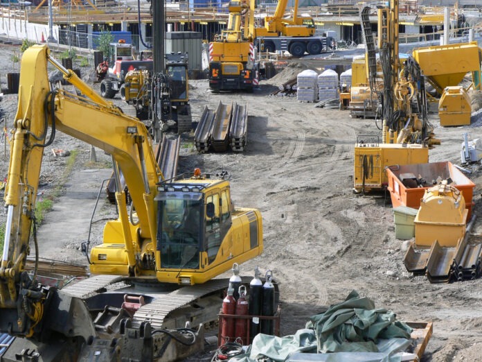 Zahlreiche Bauarbeiter, Geräte und Maschinen arbeiten auf einer Baustelle.