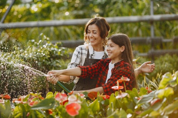 Mutter und Tochter wässern Garten mit Gartenschlauch